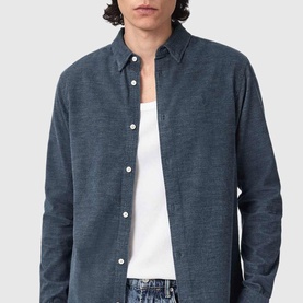 Model wearing All Saints moonstone blue button-up shirt with point collar, styled with white vest and blue jeans.