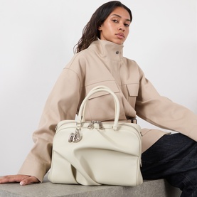 Model carrying Marc Jacobs The Wave Top Handle Bag in bone leather, silver-tone hardware, styled with a beige oversized jacket and dark trousers.