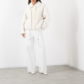 Model wearing Max Mara Sportmax ecru faux shearling zip-up coat, styled with white wide-leg trousers and white heels.