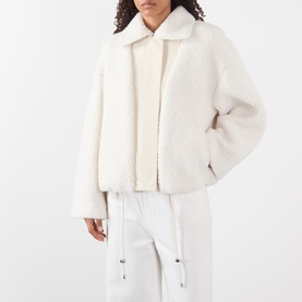Model wearing Max Mara Sportmax ecru faux shearling jacket with spread collar, styled with white drawstring trousers and cream roll-neck
