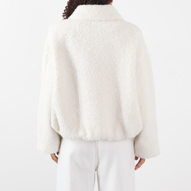 Model wearing Max Mara Sportmax ecru faux shearling cropped coat, back view, styled with white wide-leg trousers