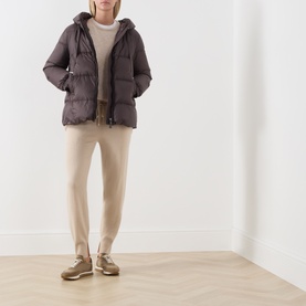 Model wearing Max Mara Cube dark brown hooded quilted down jacket, styled with cream knitwear, beige trousers and gold trainers.