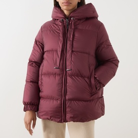 Model wearing burgundy hooded puffer jacket with zip fastening, quilted panels, and elasticated cuffs, styled with neutral trousers
