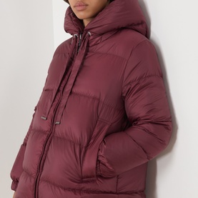Model wearing burgundy hooded puffer jacket with drawstring neckline and quilted panels, three-quarter length silhouette