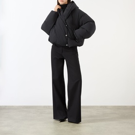 Model wearing Max Mara Sportmax black cropped puffer jacket with snap buttons, styled with black wide-leg trousers and turtleneck.