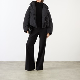 Model wearing Max Mara Sportmax black oversized puffer jacket with hood, styled with black wide-leg trousers and black roll-neck top.