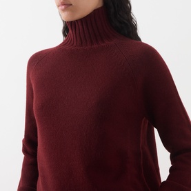 Model wearing Max Mara S Mantova Turtleneck Sweater in bordeaux wool-cashmere with chunky ribbed turtleneck collar and raglan sleeves.