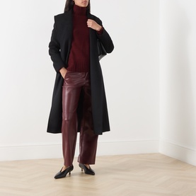 Model wearing Max Mara S Mantova Turtleneck Sweater in Bordeaux with black wool coat and burgundy leather trousers.