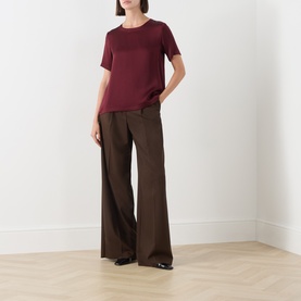 Model wearing Max Mara S Rebecca Solid T-Shirt in Bordeaux with crew neck and curved hem, styled with wide-leg brown trousers.