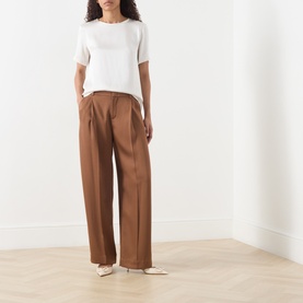 Model wearing Max Mara S ivory short-sleeve top with wide-leg brown trousers and white heeled mules.