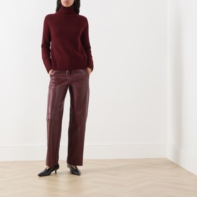 Model wearing Max Mara S Sospiro Faux Leather Straight Trousers in bordeaux, styled with a matching roll-neck jumper and black kitten heels.