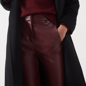 Model wearing Max Mara S Sospiro Faux Leather Straight Trousers in bordeaux, styled with a black longline coat and burgundy knit top.