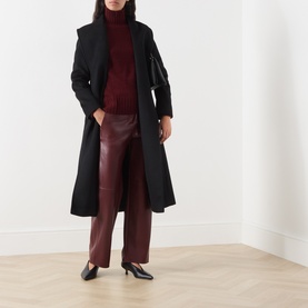 Model wearing Max Mara S Sospiro Faux Leather Straight Trousers in bordeaux, styled with black coat, burgundy roll-neck and black heels.