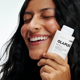 Model with Olaplex N&deg;.3 PLUS Complete Repair Treatment, holding white bottle close to face, smiling with eyes closed