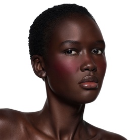 Model wearing Victoria Beckham Beauty Blusher in Fiore, a deep rosy blush applied to cheeks, with glossy nude lips.