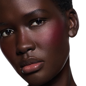 Model wearing Victoria Beckham Beauty Blusher in Fiore, a deep rosy berry shade applied to cheeks, with glossy nude lips.