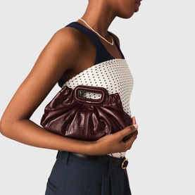 Model carrying a burgundy ruched leather clutch bag with gold-tone hardware clasp, styled with a monochrome top and navy trousers