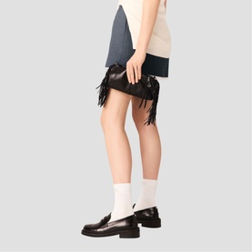 Model carrying Maje red leather fringed clutch bag with silver hardware, styled with colourblock mini skirt and black loafers
