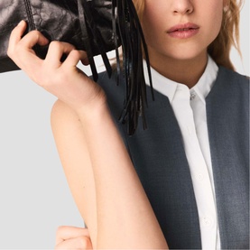 Model carrying Maje red bag with fringe detail, styled with white shirt and grey sleeveless jacket