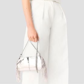 Model carrying Maje red bag with fringe detail and silver chain strap, styled with white wide-leg trousers