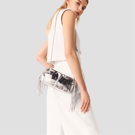 Model carrying Maje bag in silver with metallic fringe detail and chain strap, styled with white sleeveless top and wide-leg trousers