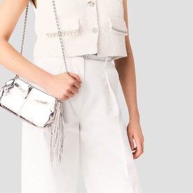 Model carrying Maje red crossbody bag with fringe detail and silver chain strap, styled with white tailored trousers and cropped jacket