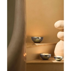 Alessi Candle Container with Lid Small in polished stainless steel, styled on wooden shelves with matching bowl and decorative sculpture.