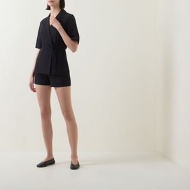Model wearing Aligne black linen blend blazer, styled with matching black shorts and flat black shoes.