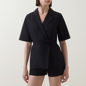 Model wearing Aligne black linen blend blazer with tie waist and short sleeves, styled with matching black shorts.
