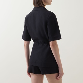 Model wearing Aligne black linen blend blazer, rear view, shown with matching black shorts, belted waist detail visible.