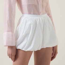 Model wearing Aligne Paulo Bubble Shorts in white with bubble hem, styled with a light pink long-sleeve shirt.