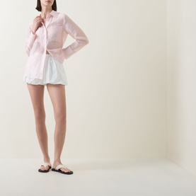 Model wearing Aligne Paulo Bubble Shorts in white poplin with bubble hem, styled with a pink shirt and flat sandals.