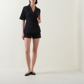 Model wearing Aligne black linen-blend wrap top and matching black mini shorts, styled with black flat leather mules.