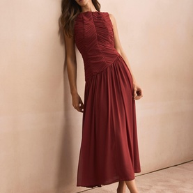 Model wearing a sleeveless ruched midi dress in deep red with gathered bodice detail and flared skirt