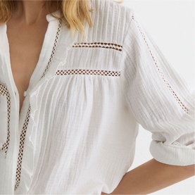 Model wearing Reiss white broderie lace-trim blouse with V-neckline, crochet panel detail, and relaxed three-quarter sleeves.