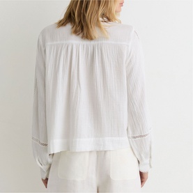 Model wearing Reiss white textured blouse, back view, with lace trim detailing on sleeves and hem, styled with white wide-leg trousers