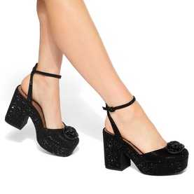 Model wearing Kurt Geiger London black glitter platform heels with ankle strap and floral toe detail, chunky block heel