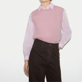 Model wearing Jigsaw pink knit vest over a light pink shirt, styled with dark brown wide-leg trousers.
