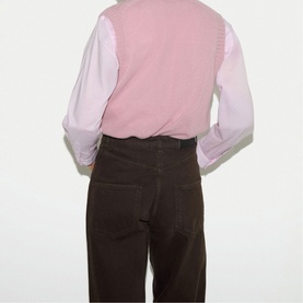 Model wearing Jigsaw pink knitted vest over a white long-sleeve shirt, styled with dark brown wide-leg trousers, back view.