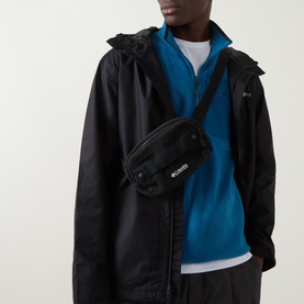 Model carrying Columbia Helvetia&trade; Sherpa Bum Bag in black, worn crossbody, with adjustable strap and logo badge, styled with black jacket and blue