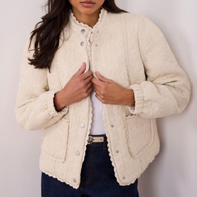 Model wearing Mint Velvet Floral Quilted Jacket in white with lace trim, scallop hem detail and popper fastenings, styled with dark jeans.