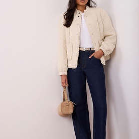 Model wearing Mint Velvet White Floral Quilted Jacket with high neckline and lace trim, styled with dark wide-leg jeans and small tan bag.