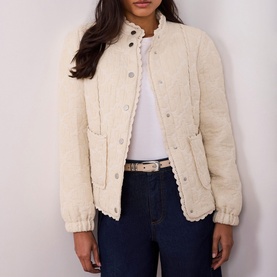 Model wearing Mint Velvet Floral Quilted Jacket in white with lace trim, styled with white shirt, dark jeans and woven belt.