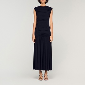 Model wearing Sandro Womens French Dress in black, ruched bodice, pleated maxi skirt, cap sleeves, styled with strappy sandals.
