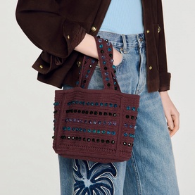 Model carrying Sandro brown embellished mini tote bag with sequin stripe detail and stud trim, styled with blue jeans and brown suede jacket