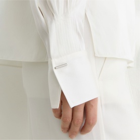 Model wearing Reiss white dress, close-up of structured cuff detail with silver bar fastening and pleated bib front.