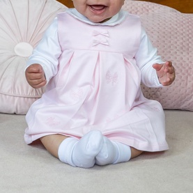 Baby wearing Emile Et Rose pink dress with bow detail and embroidery, styled with white long-sleeve bodysuit and socks