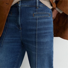 Model wearing Reiss mid blue jeans with front seam detail, styled with a brown jacket