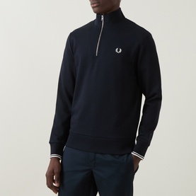 Model wearing Fred Perry Laurel Wreath Logo Half-Zip Sweatshirt in navy, with funnel neck, half-zip and ribbed trims. Styled with navy trousers.