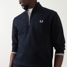 Model wearing Fred Perry Laurel Wreath Logo Half-Zip Sweatshirt in navy, with funnel neck, half-zip and ribbed trims, styled over white crew neck tee